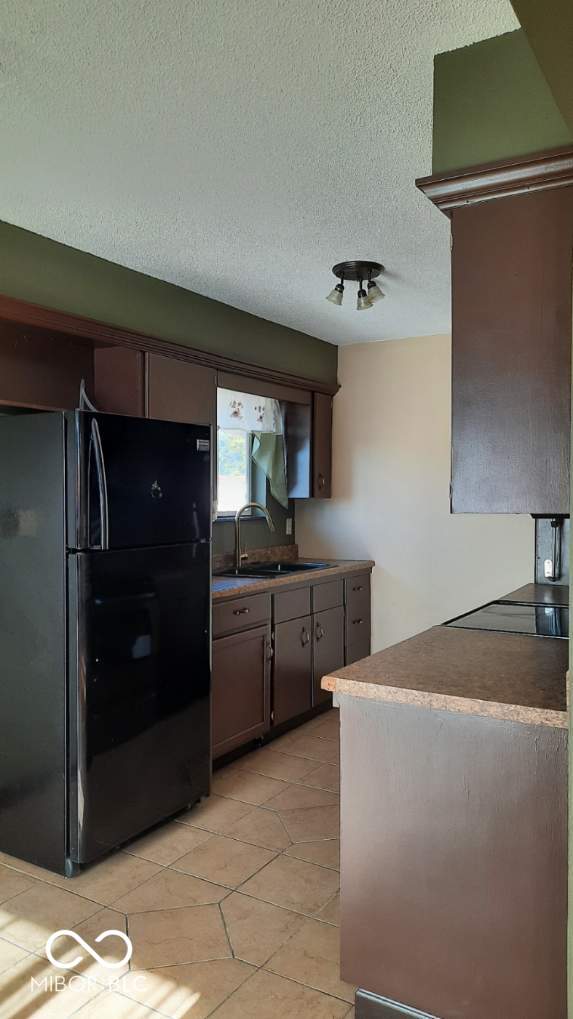 kitchen with dark brown cabinetry, light tile patterned floors, sink, a textured ceiling, and black appliances