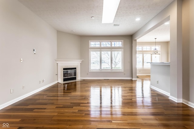 unfurnished living room featuring an inviting chandelier, dark wood-type flooring, a fireplace, and a textured ceiling