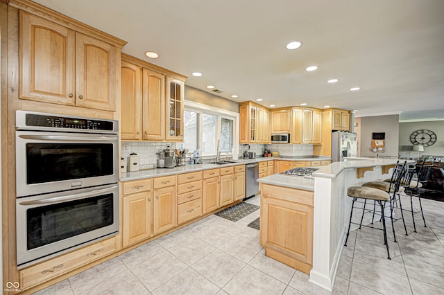 kitchen with glass insert cabinets, stainless steel appliances, light countertops, light brown cabinetry, and a kitchen bar