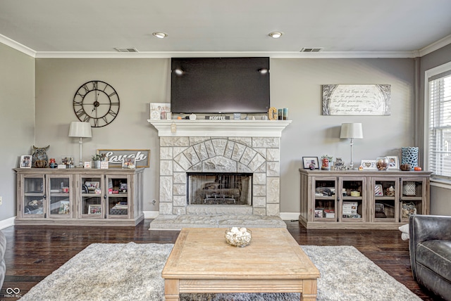 living room with ornamental molding, visible vents, a fireplace with raised hearth, and wood finished floors