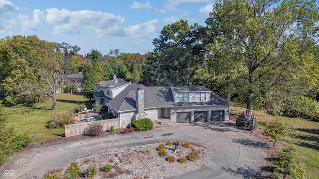 view of front of home featuring driveway, stone siding, a chimney, fence, and a front lawn