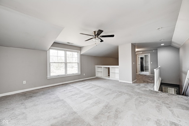 unfurnished living room with ceiling fan, carpet floors, visible vents, baseboards, and vaulted ceiling