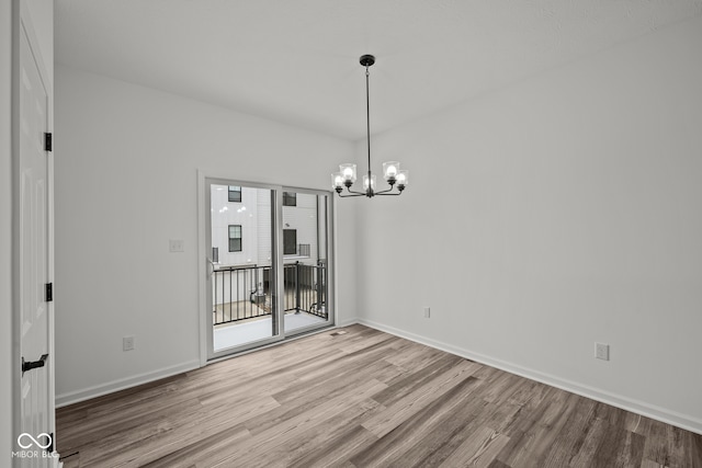 unfurnished dining area featuring wood-type flooring and an inviting chandelier