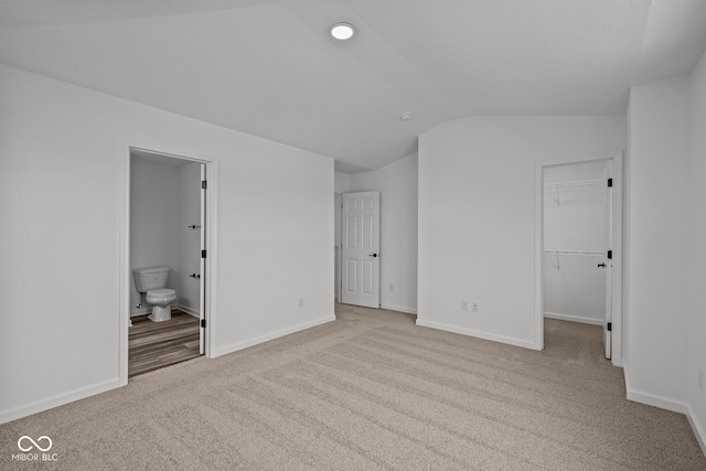 unfurnished bedroom featuring ensuite bathroom, a spacious closet, light carpet, and lofted ceiling