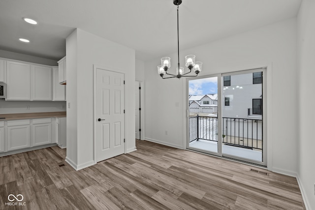 unfurnished dining area with a notable chandelier and light wood-type flooring