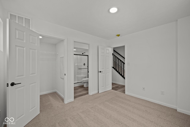 unfurnished bedroom with ensuite bath, a closet, and light colored carpet