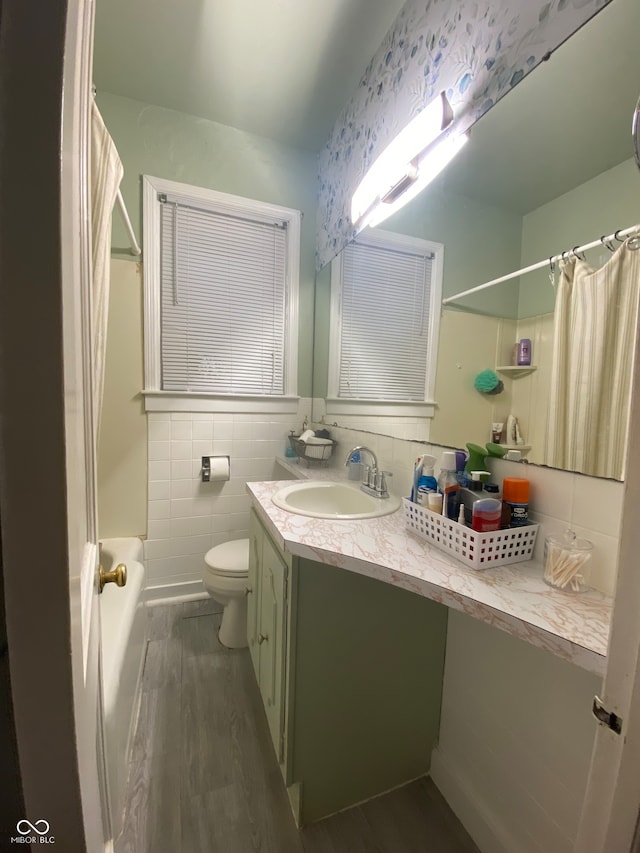 full bathroom with shower / tub combo, vanity, hardwood / wood-style flooring, tile walls, and toilet