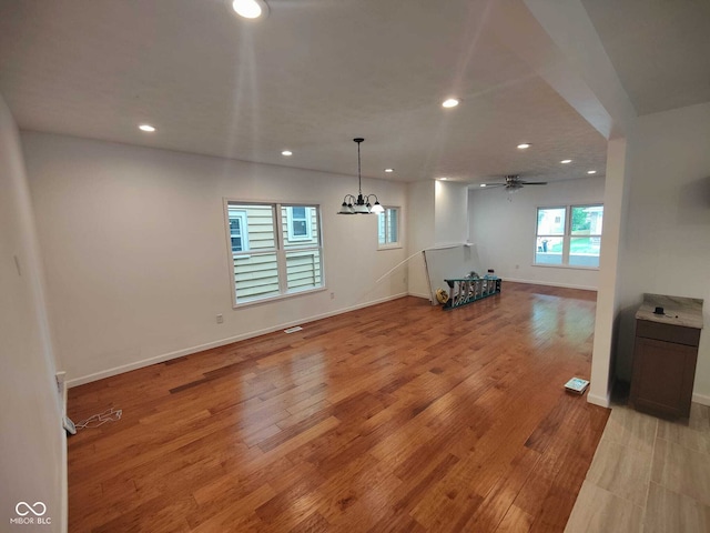 unfurnished living room featuring ceiling fan with notable chandelier and light wood-type flooring