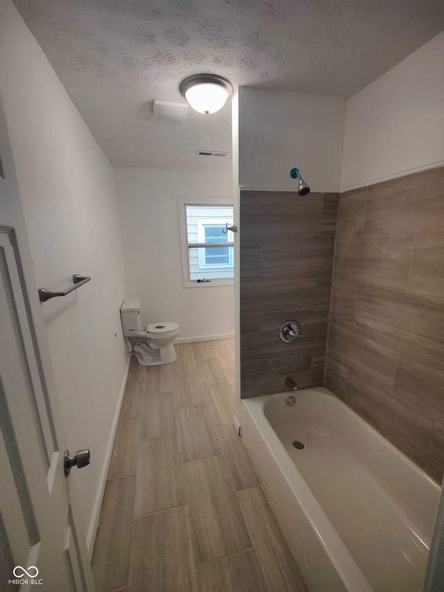 bathroom with tiled shower / bath, a textured ceiling, and toilet