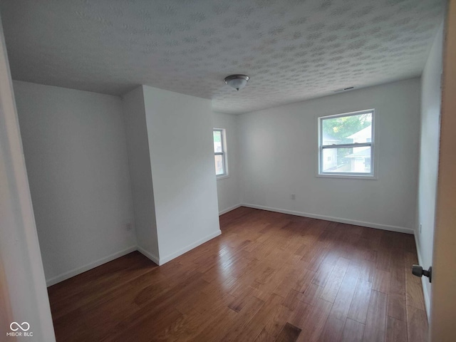 spare room featuring a textured ceiling, a healthy amount of sunlight, and dark hardwood / wood-style flooring