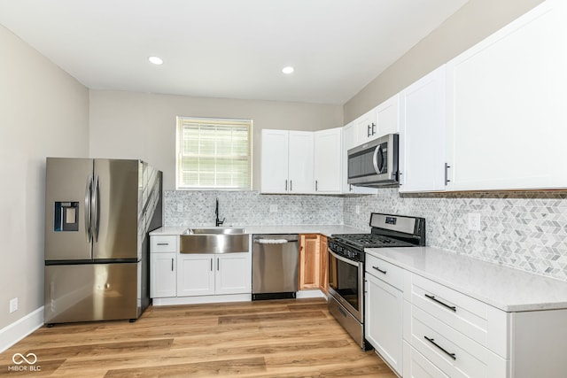 kitchen featuring stainless steel appliances, white cabinets, sink, and light wood-type flooring