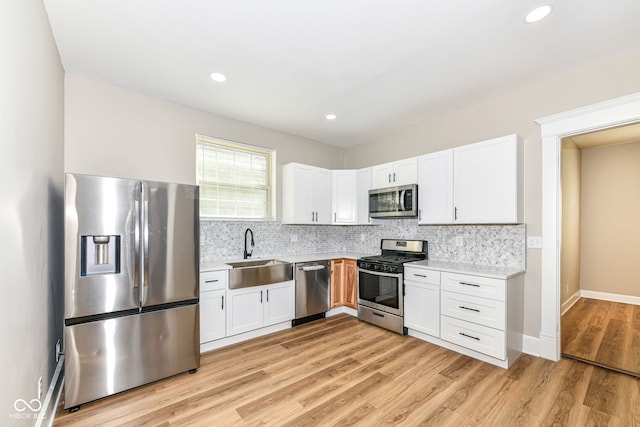 kitchen featuring decorative backsplash, stainless steel appliances, white cabinets, sink, and light hardwood / wood-style flooring