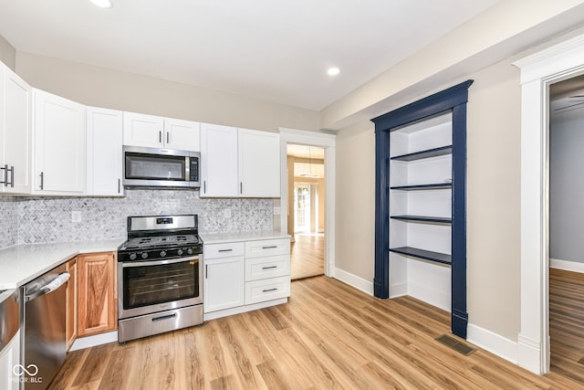 kitchen with stainless steel appliances, decorative backsplash, light wood-type flooring, and white cabinetry