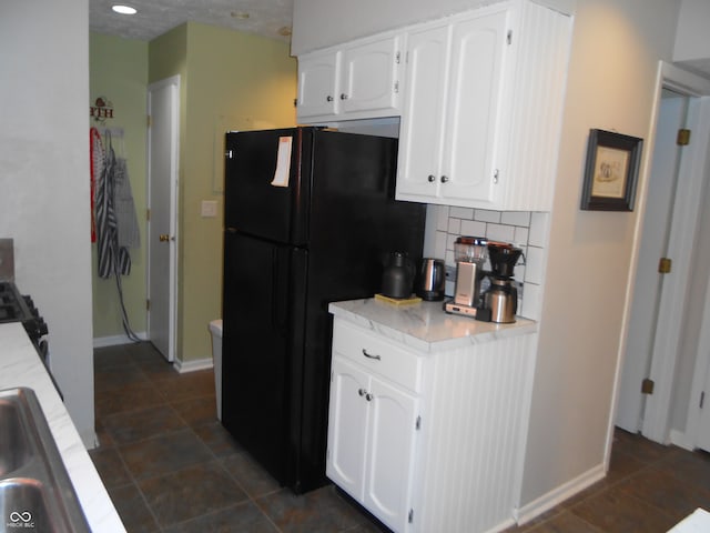 kitchen with tasteful backsplash, black fridge, and white cabinetry