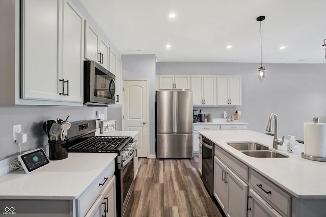 kitchen with dark wood-type flooring, white cabinets, hanging light fixtures, sink, and appliances with stainless steel finishes