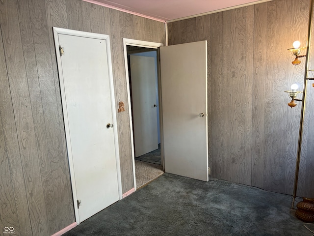 unfurnished bedroom featuring wood walls, dark carpet, and a closet