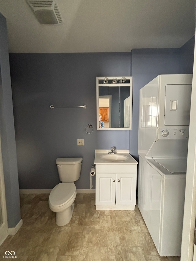 bathroom featuring stacked washer / dryer, vanity, and toilet