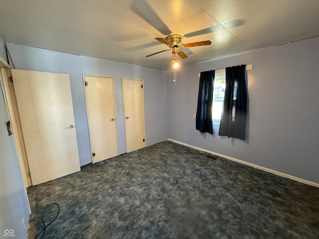 unfurnished bedroom featuring ceiling fan, two closets, and dark carpet