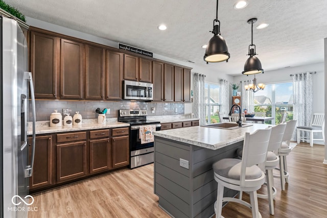 kitchen with sink, hanging light fixtures, light hardwood / wood-style flooring, appliances with stainless steel finishes, and a center island with sink