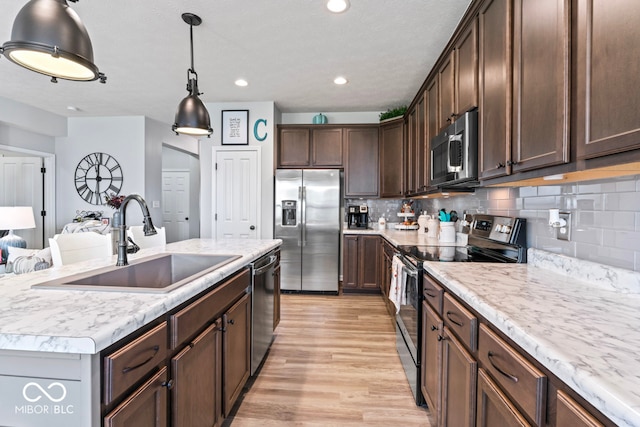 kitchen with decorative backsplash, sink, light hardwood / wood-style floors, appliances with stainless steel finishes, and a center island with sink