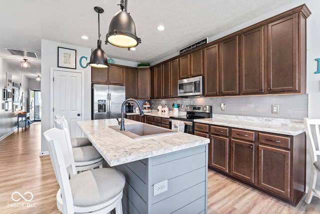 kitchen with dark brown cabinetry, sink, decorative light fixtures, light hardwood / wood-style flooring, and stainless steel appliances