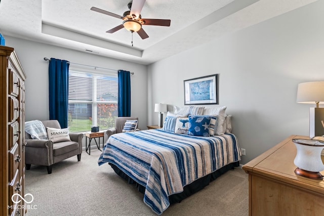 bedroom featuring a textured ceiling, ceiling fan, carpet, and a raised ceiling