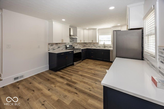 1666 Union St, Indianapolis, IN 46225 - kitchen with white cabinetry, decorative backsplash, appliances with stainless steel finishes, wall chimney exhaust hood, and wood finished floors