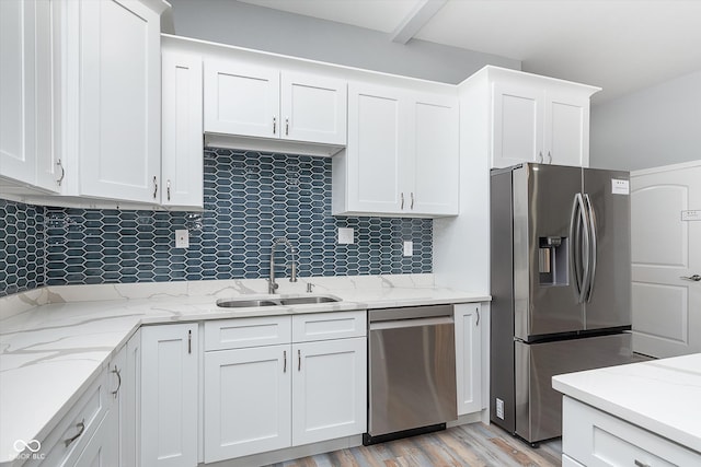 kitchen with backsplash, appliances with stainless steel finishes, white cabinetry, light wood-type flooring, and sink