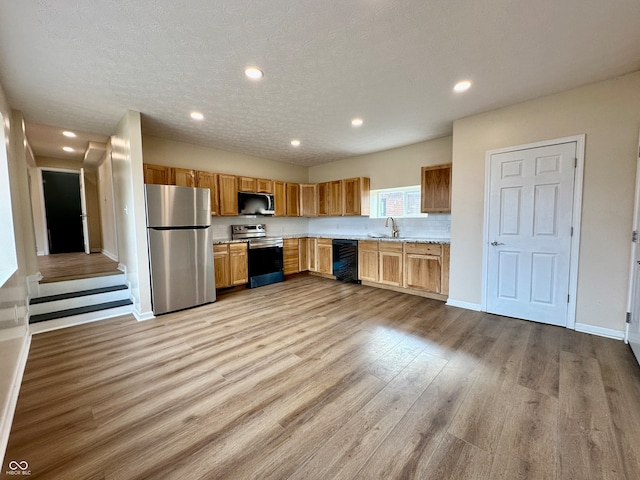 kitchen featuring beverage cooler, light wood-type flooring, a textured ceiling, and appliances with stainless steel finishes