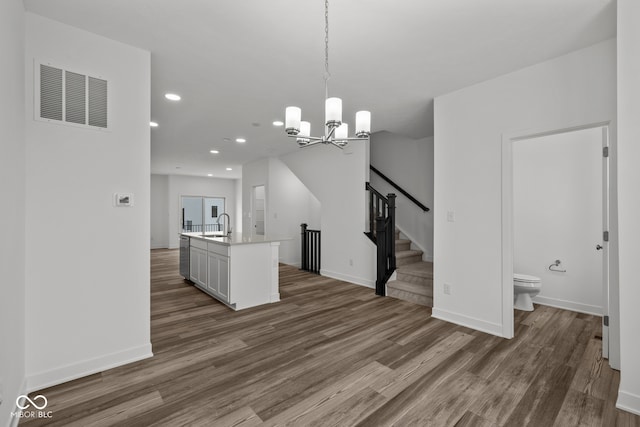 kitchen with a chandelier, an island with sink, dark hardwood / wood-style floors, and decorative light fixtures