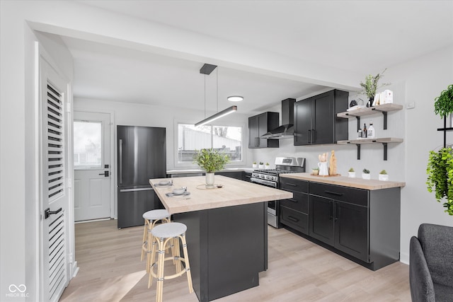 kitchen with a kitchen breakfast bar, a wealth of natural light, wall chimney range hood, and appliances with stainless steel finishes