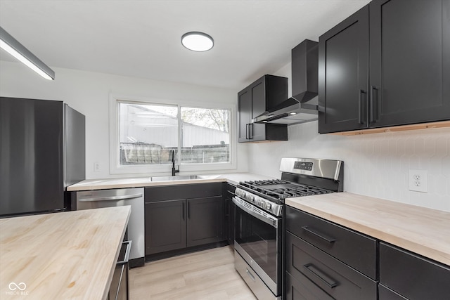 kitchen with stainless steel appliances, wooden counters, wall chimney exhaust hood, and sink