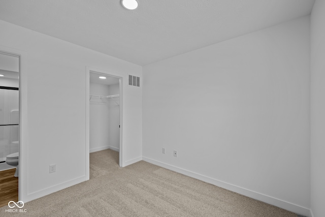 unfurnished bedroom with ensuite bathroom, light colored carpet, a spacious closet, and a closet