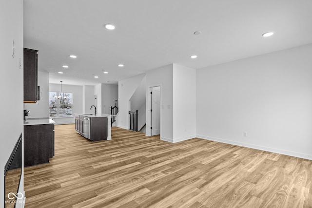 kitchen with sink, an inviting chandelier, a center island with sink, dark brown cabinets, and light wood-type flooring