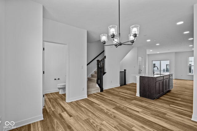 kitchen with sink, pendant lighting, a center island with sink, dark brown cabinets, and hardwood / wood-style flooring