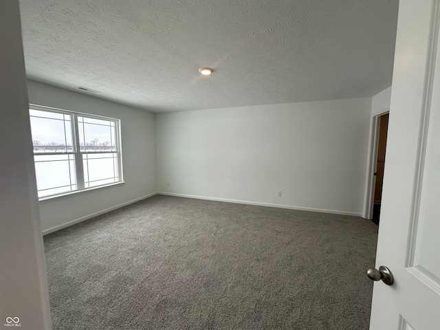 spare room featuring dark carpet and a textured ceiling