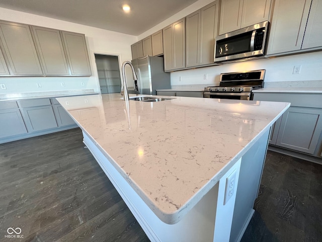 kitchen with light stone counters, sink, stainless steel appliances, and a center island with sink