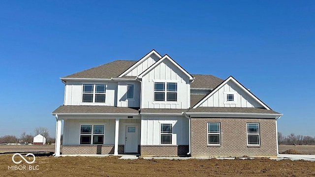 modern farmhouse style home with board and batten siding, covered porch, brick siding, and a shingled roof