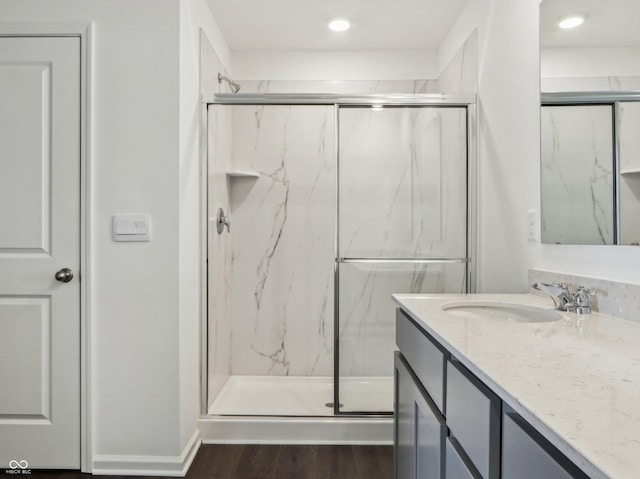 full bath with baseboards, vanity, a marble finish shower, and wood finished floors