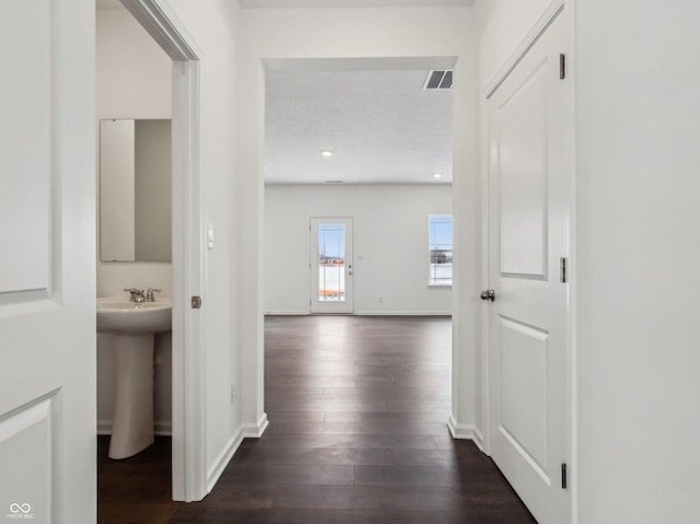 hall featuring visible vents, dark wood finished floors, a sink, and baseboards