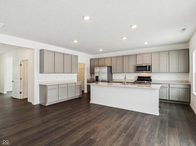 kitchen featuring dark wood-style flooring, a kitchen island with sink, stainless steel appliances, light countertops, and a sink