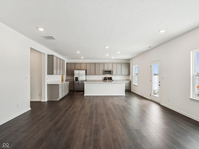 kitchen with a kitchen island with sink, visible vents, open floor plan, light countertops, and appliances with stainless steel finishes