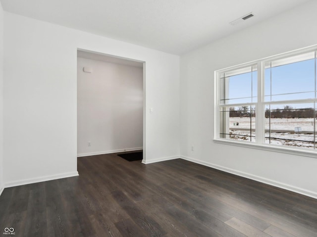 empty room with dark wood-type flooring, visible vents, and baseboards