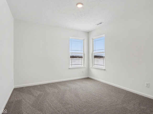 carpeted spare room featuring visible vents, baseboards, and a textured ceiling