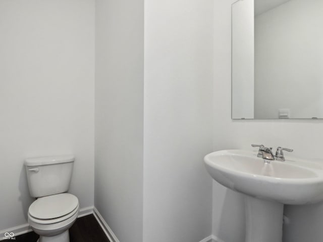 half bath with a sink, toilet, baseboards, and wood finished floors