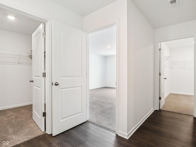 corridor featuring dark colored carpet, visible vents, dark wood finished floors, and baseboards