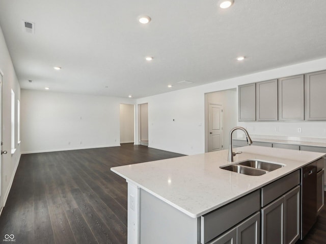 kitchen with a kitchen island with sink, dark wood-type flooring, a sink, gray cabinets, and light stone countertops