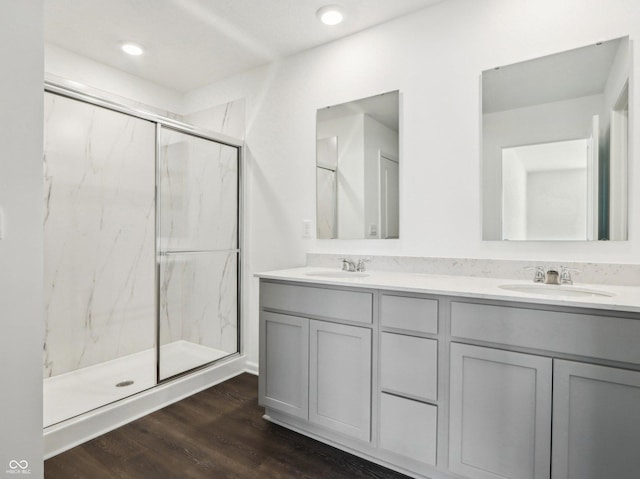 full bath with double vanity, a marble finish shower, a sink, and wood finished floors