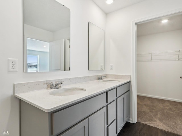 bathroom with double vanity, a sink, a walk in closet, and baseboards