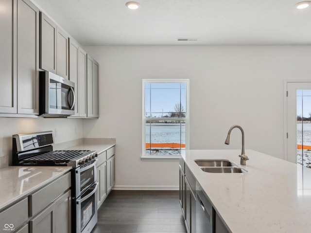 kitchen featuring appliances with stainless steel finishes, dark wood-style flooring, light stone countertops, gray cabinetry, and a sink